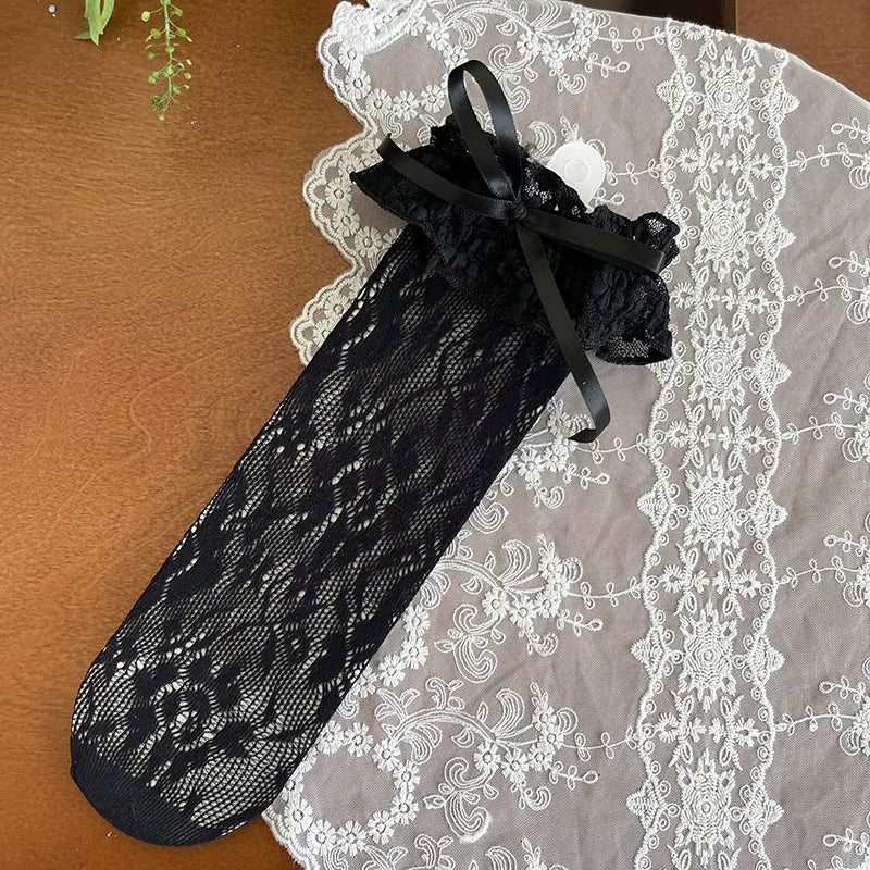 White lace mid-calf slouch socks with ruffled cuffs and ribbon ties styled with pale bow flats.