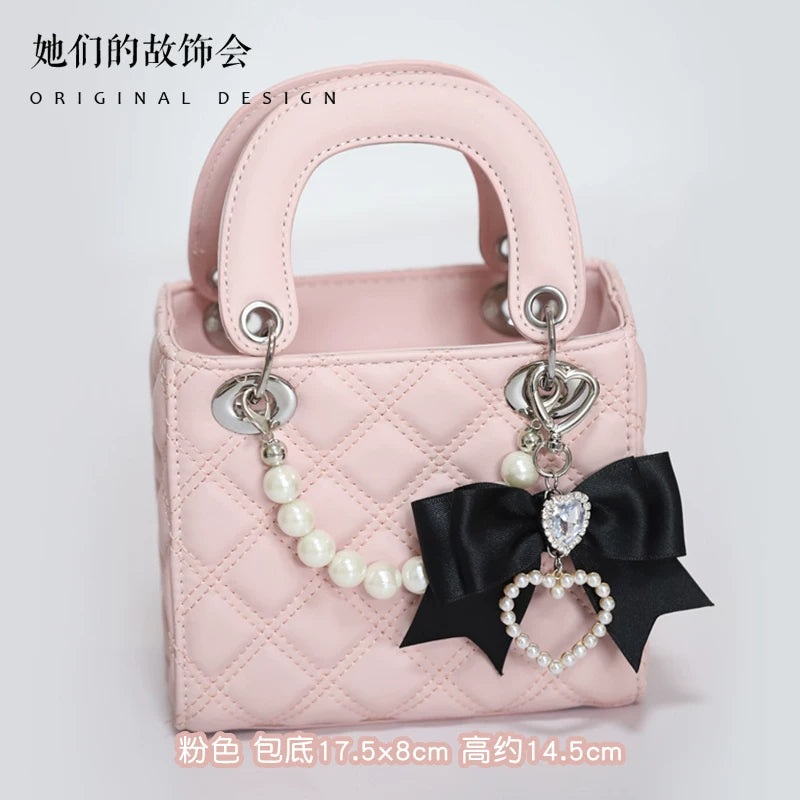 Pink quilted top-handle bag with pearl chain and bow-and-heart charm.