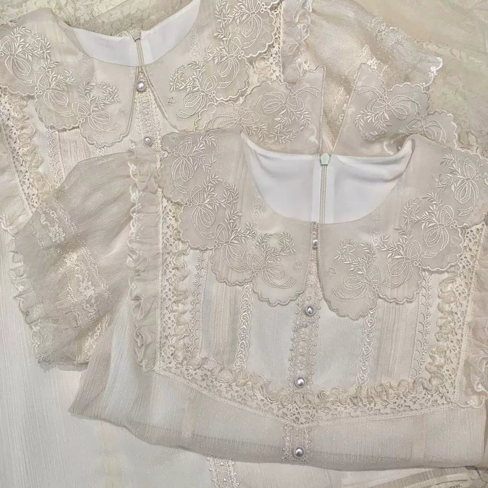 White short-sleeve blouse with lace bib, bow motifs, and round buttons laid flat.
