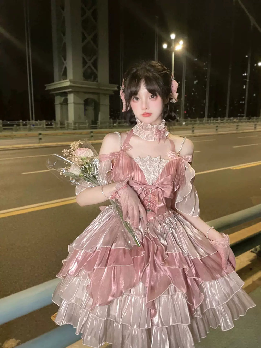 Pink JSK dress with a large bow and layered ruffles shown on a model at night.