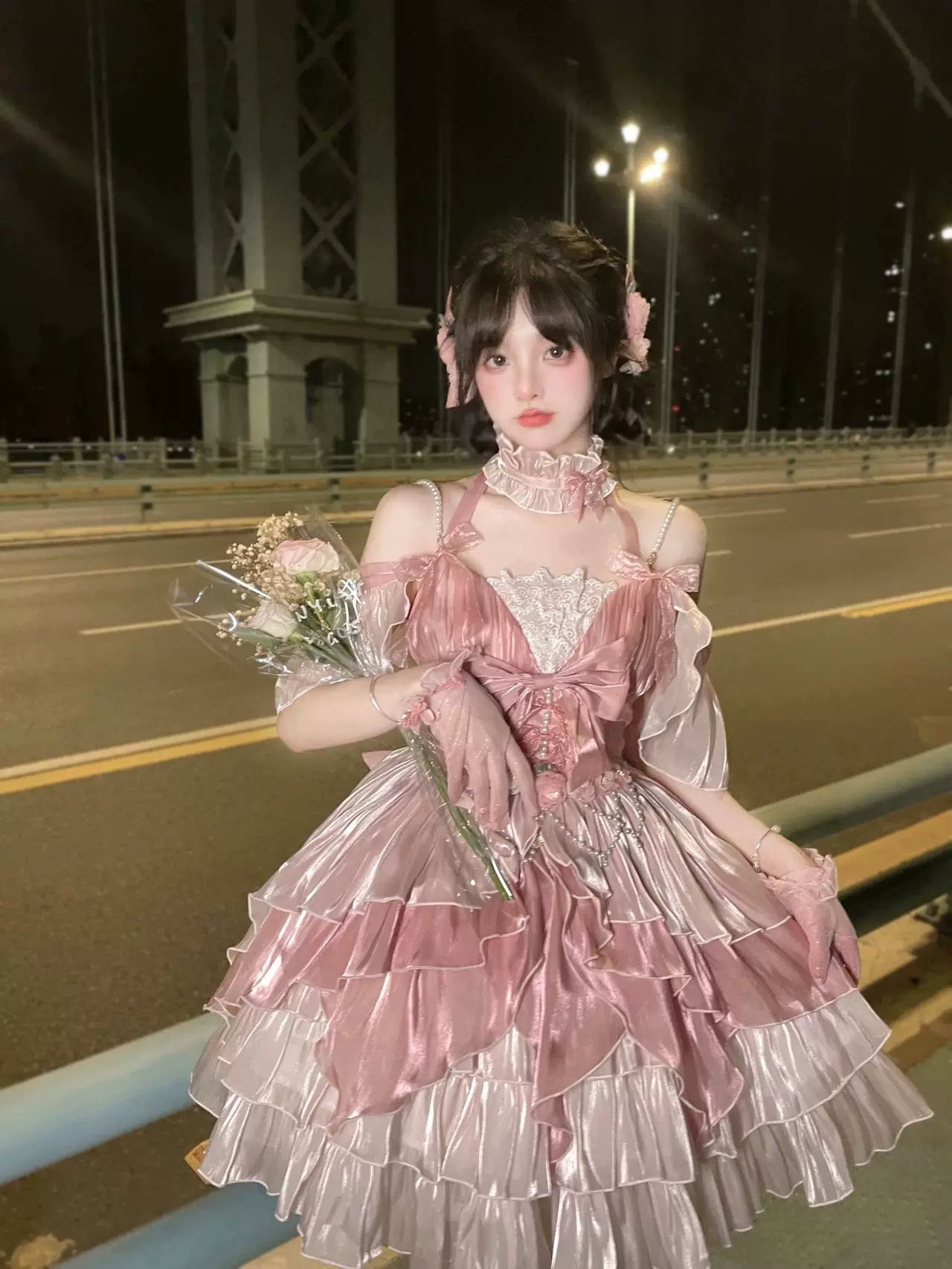 Pink JSK dress with a large bow and layered ruffles shown on a model at night.