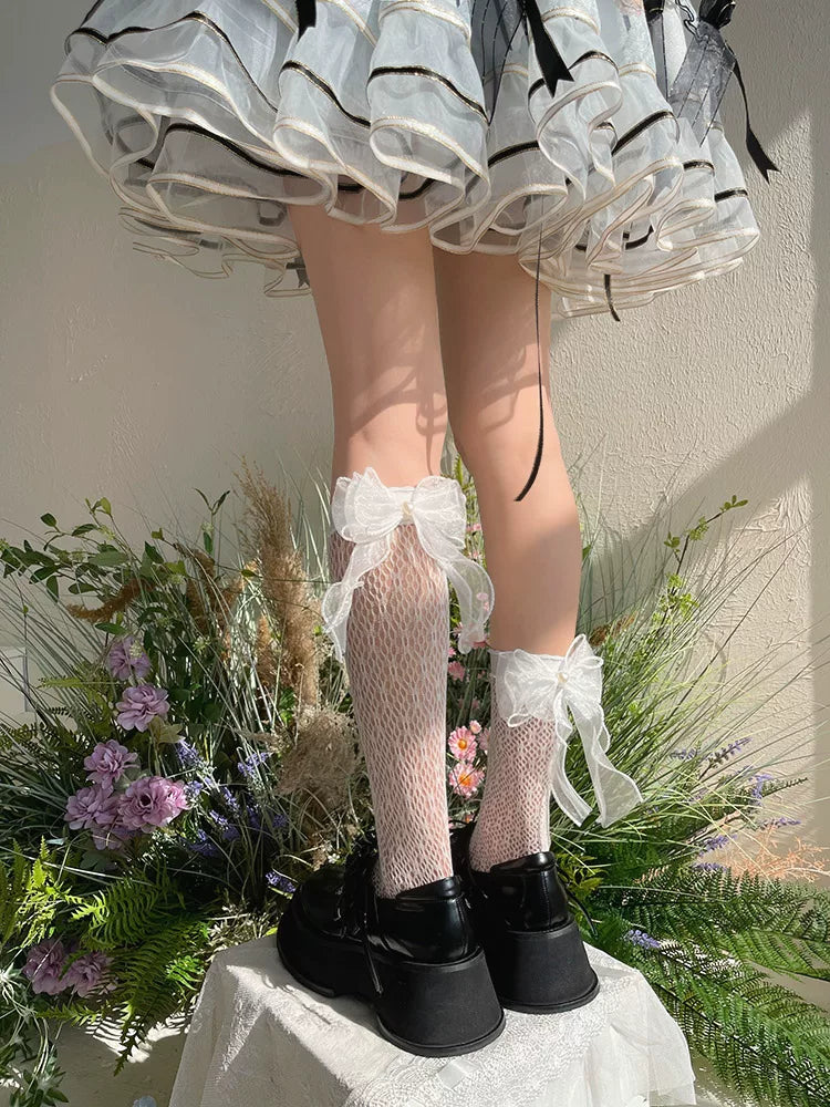 Model wearing black lace mid-calf socks with large ribbon bows and platform shoes.