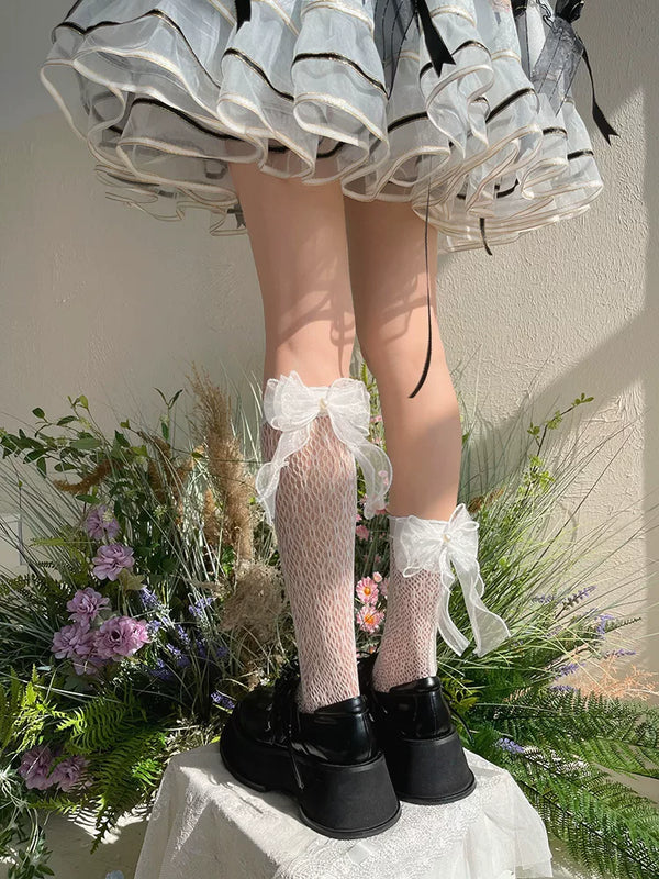 Model wearing black lace mid-calf socks with large ribbon bows and platform shoes.