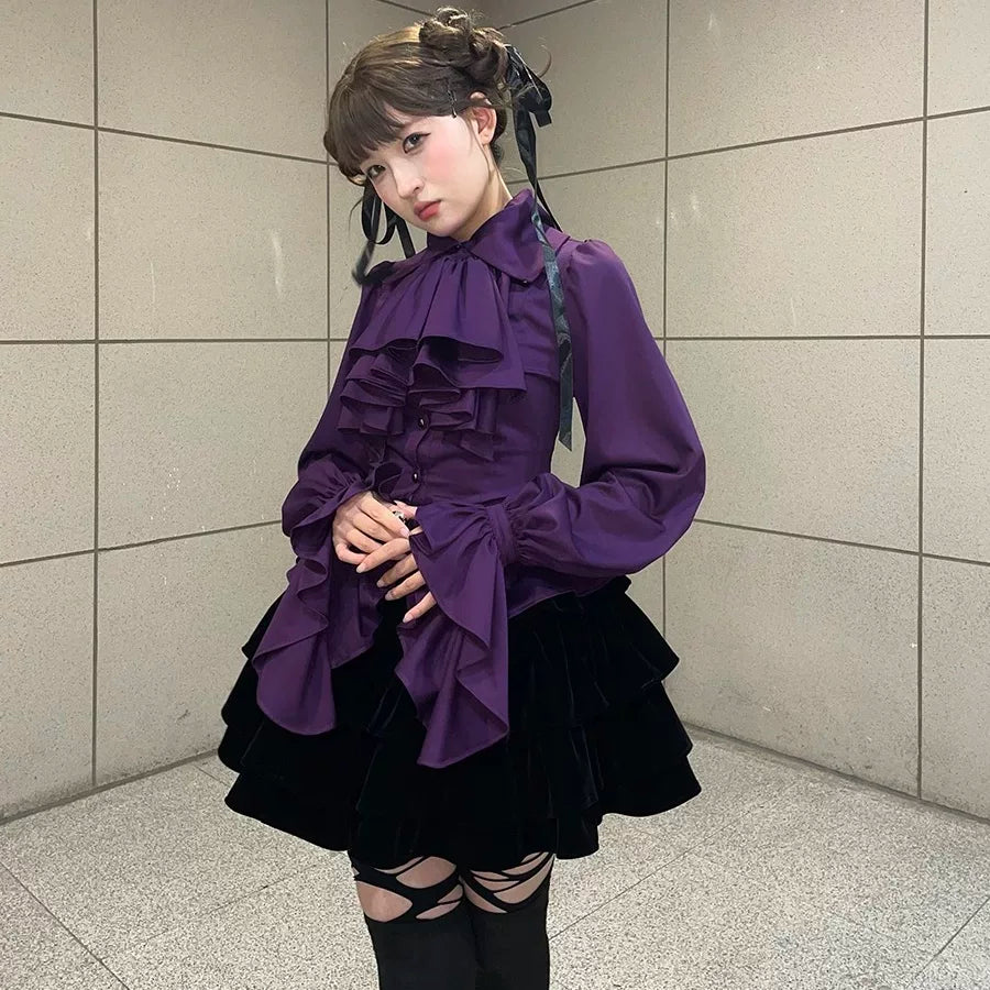 Model wearing a dark-toned long-sleeve blouse with layered ruffles and gathered cuffs.