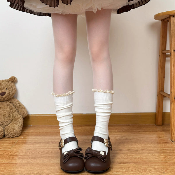 Model wearing off-white gathered calf socks with lace cuffs beneath a brown plaid skirt.