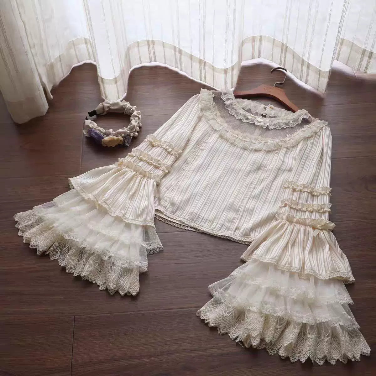 Natural-colour vertically striped blouse with lace collar and layered sleeves laid flat.