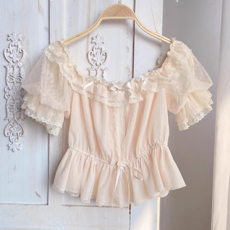 Apricot short-sleeve blouse with puff sleeves, lace ruffles, and a tied waist on a hanger.