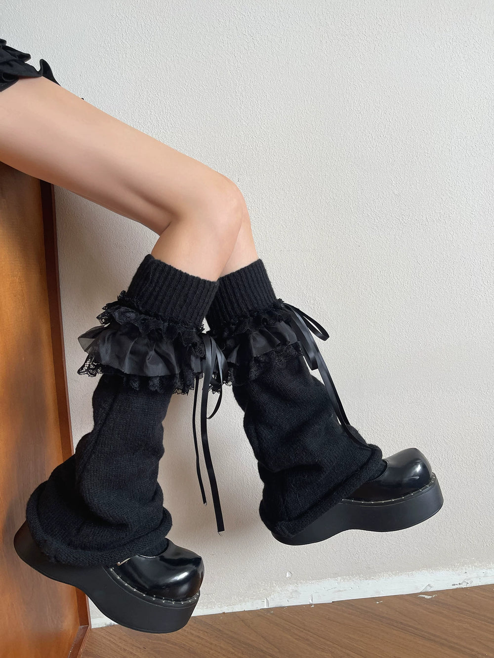 Black knit sock covers with tiered lace ruffles and ribbon ties worn with platform shoes.