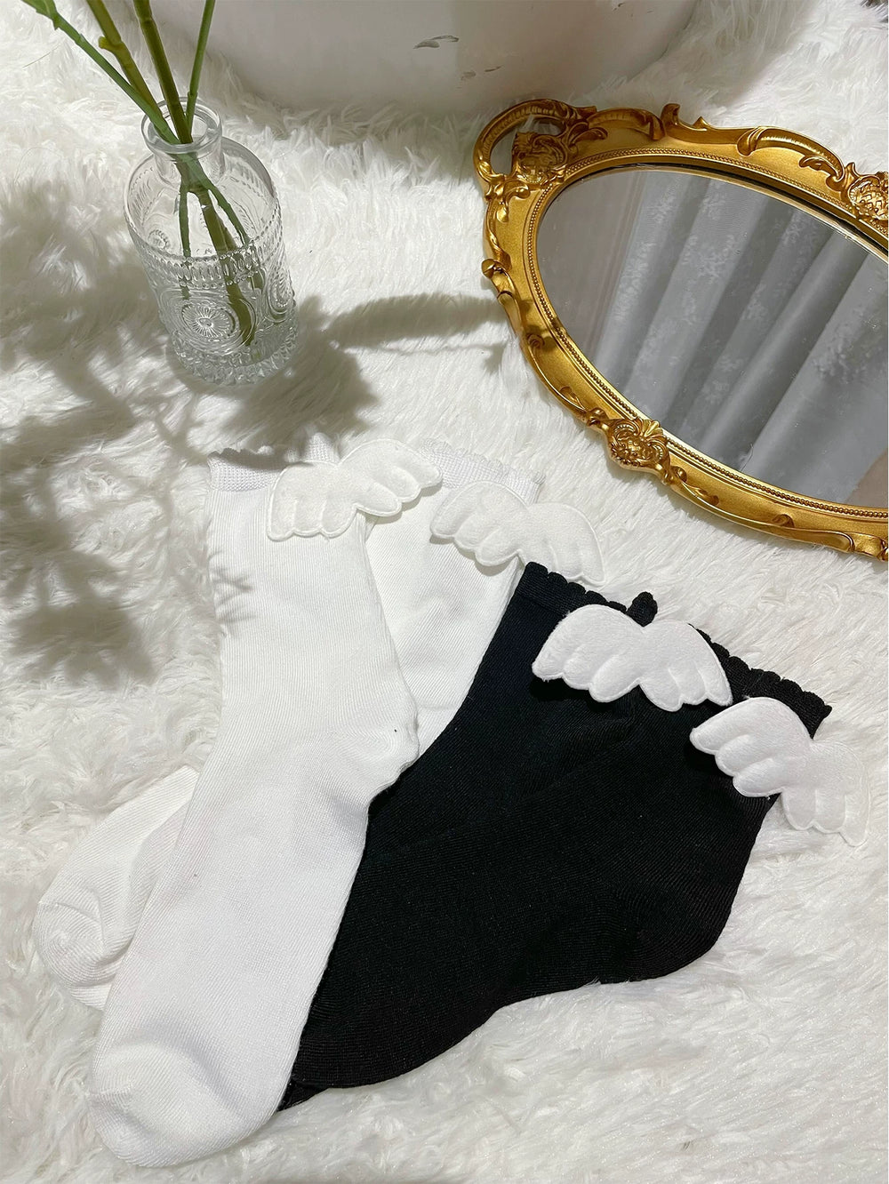 White and black ankle socks with white angel-wing appliqués arranged on a white surface.