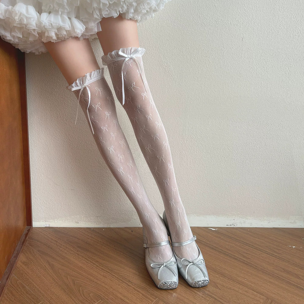 Sock Noble white patterned over-the-knee socks with ruffled cuffs and ribbon ties, shown with silver shoes on a model.