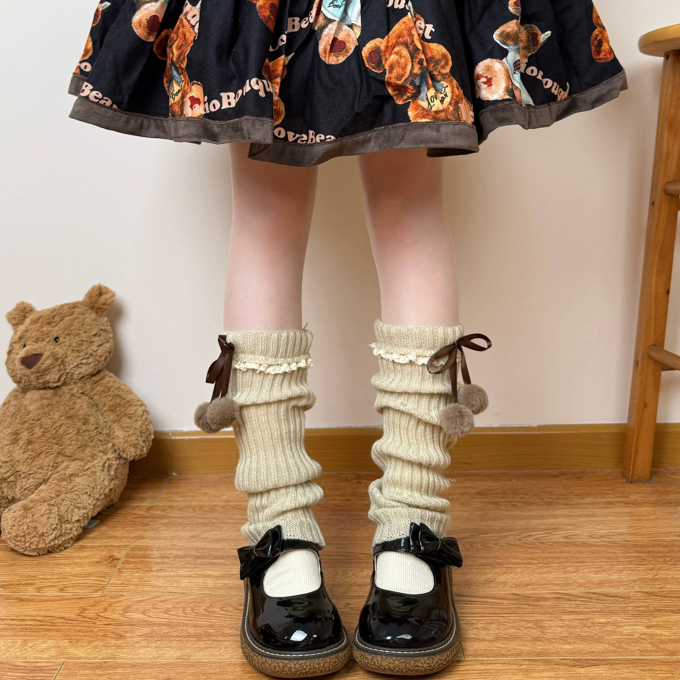 White scrunched knit leg-warmer socks with lace trim, ribbon ties and pom-poms shown on a model.