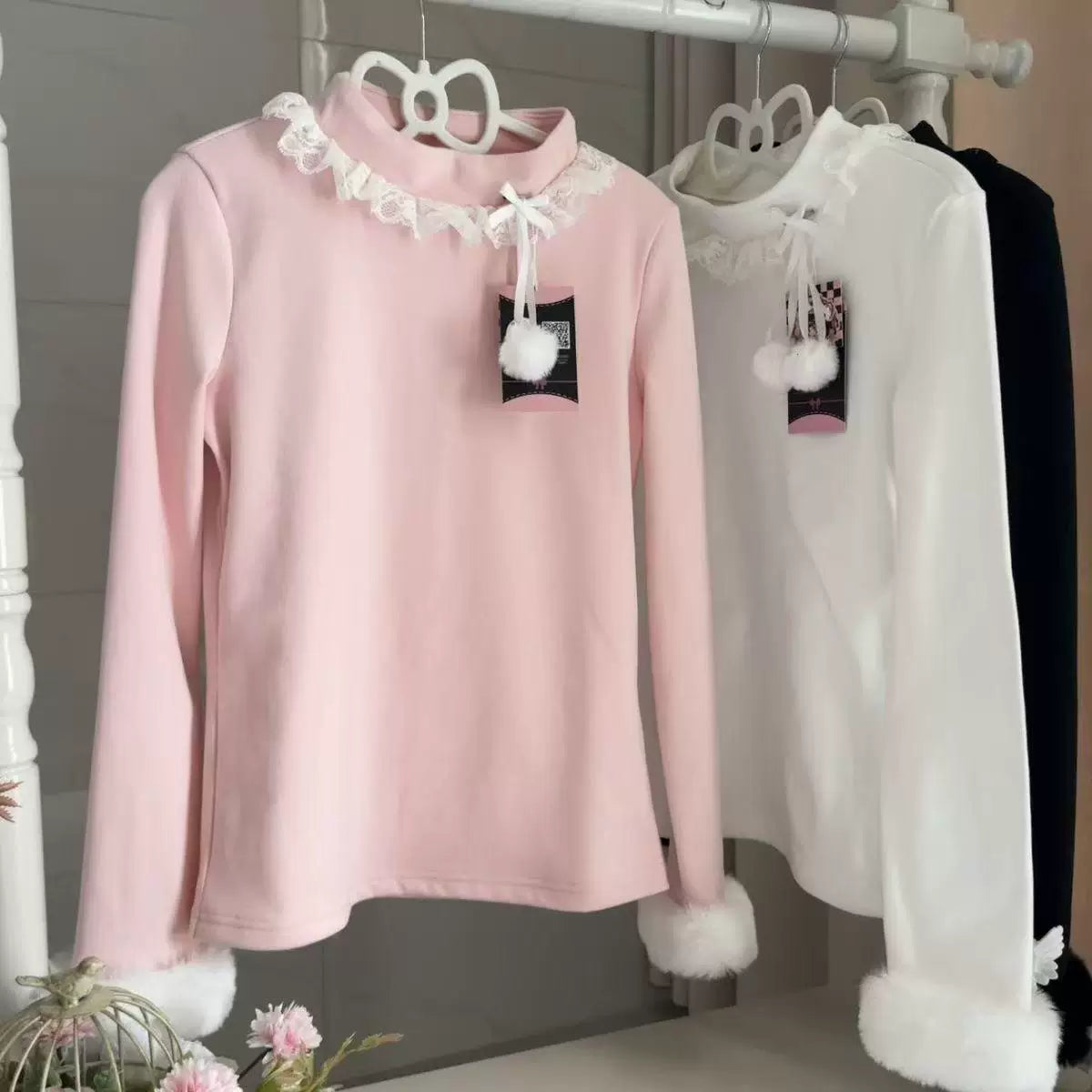 White long-sleeve base layer top with a lace collar and furry cuffs displayed on a rack.