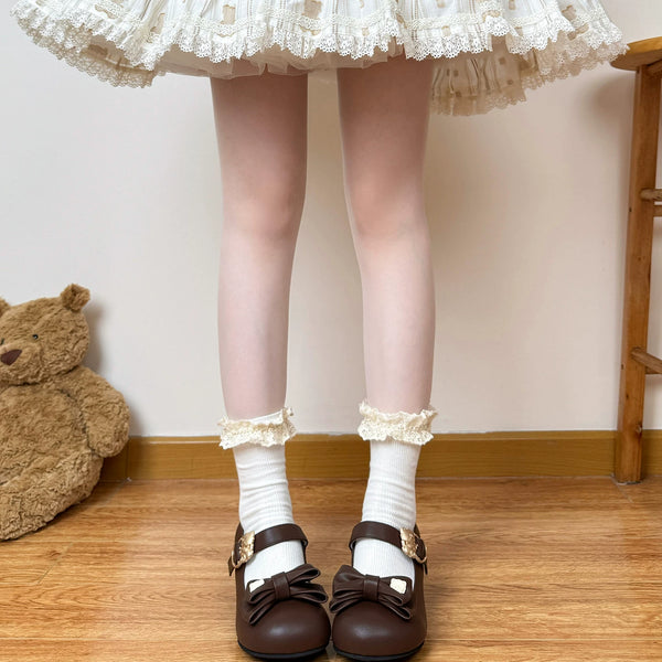 White lace-cuff mid-calf socks styled with brown bow shoes beneath a ruffled skirt.