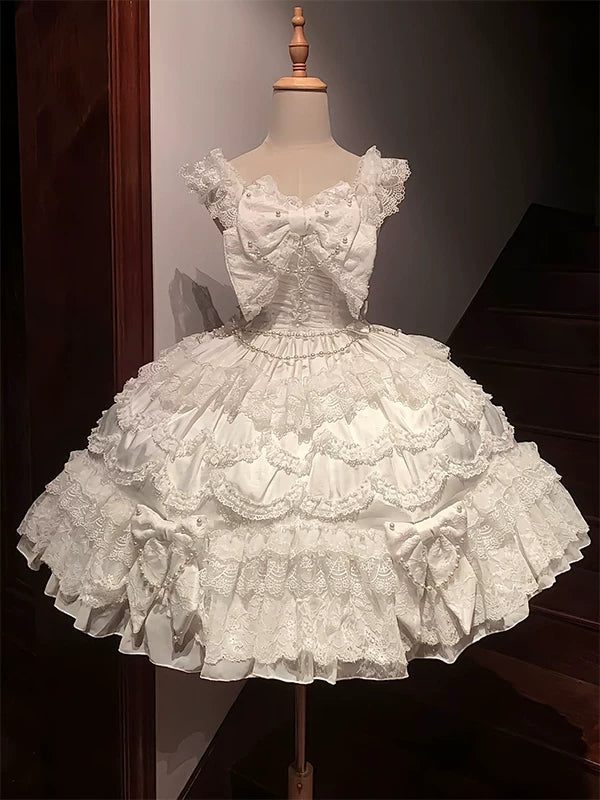 White tiered JSK dress with an oversized lace bow, pearl accents and waist chain on a mannequin.