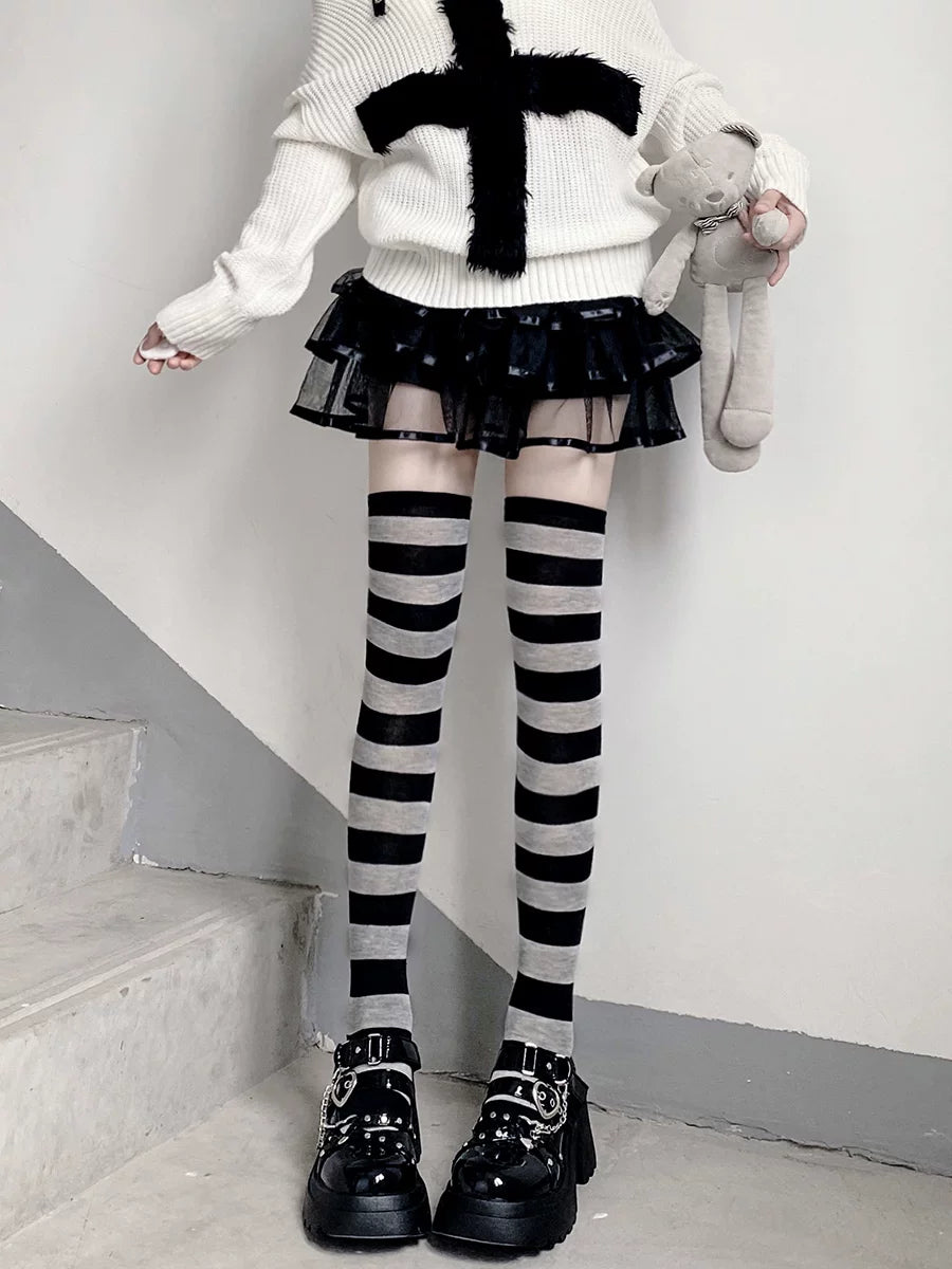 Model wearing black and gray horizontal striped over-the-knee socks with a black layered skirt