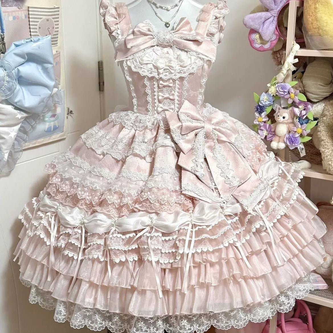 Pink embroidered JSK with layered lace, bows and a tiered skirt displayed on a mannequin.