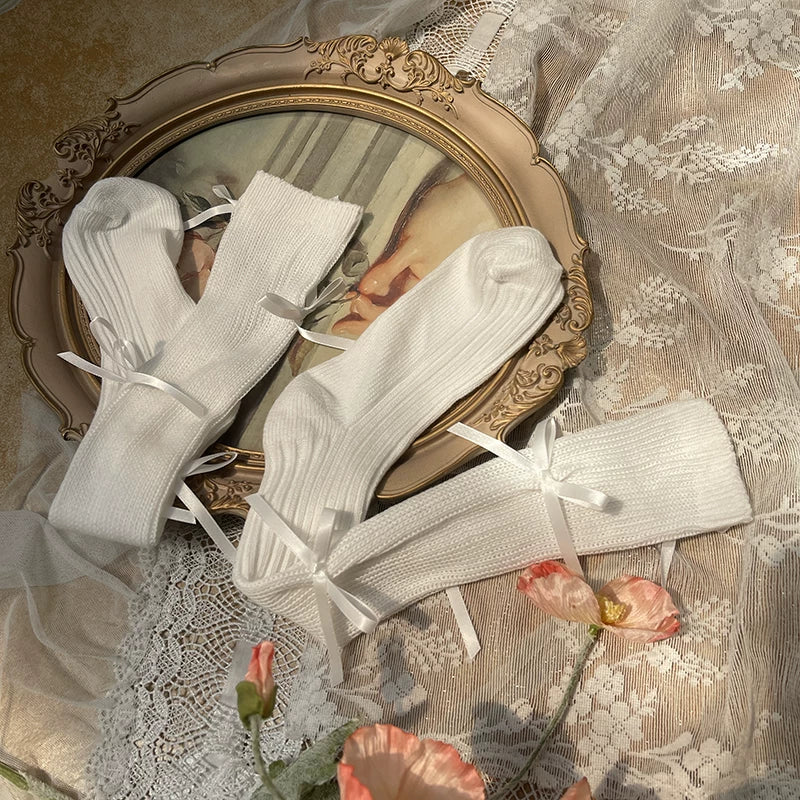 Five color options of ribbon-bow slouch mid-calf socks arranged on lace with a vintage mirror.