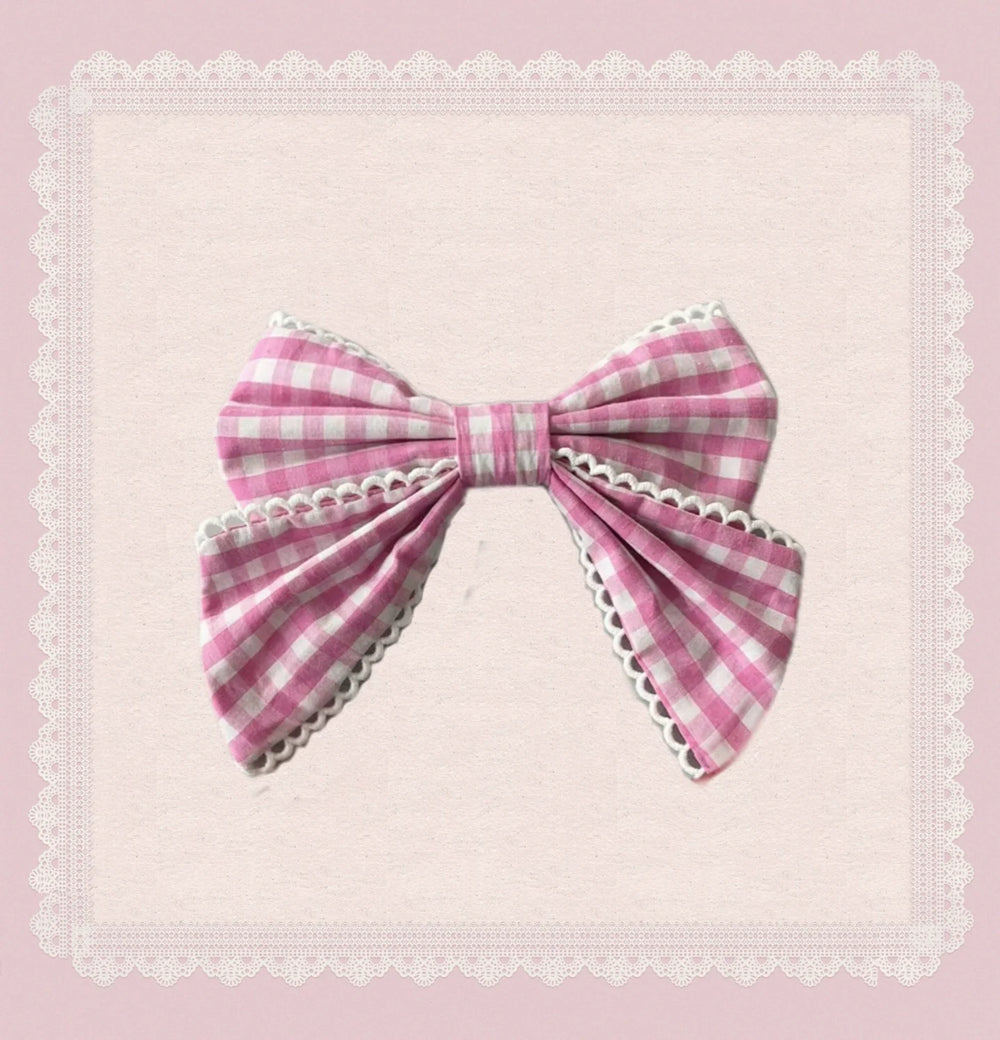 Pink gingham bow with white lace edging on a pale pink background.