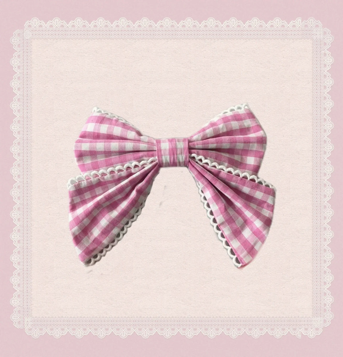 Pink gingham bow with white lace edging on a pale pink background.