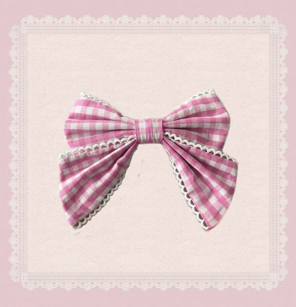 Pink gingham bow with white lace edging on a pale pink background.