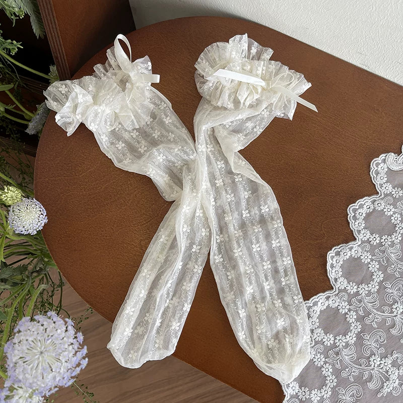 White semi-transparent floral lace socks with ruffled cuffs styled with white Mary Jane shoes.