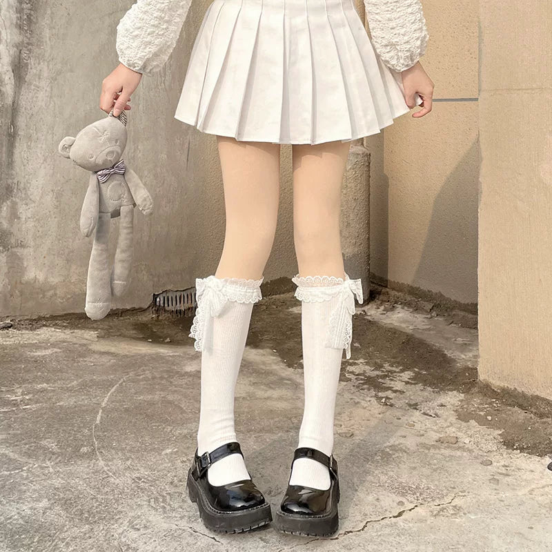 Black tube socks with white lace cuffs and bow ties styled below a black skirt