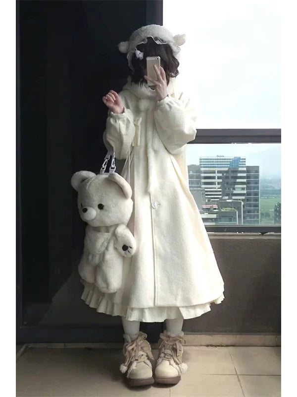 Cream hooded long woolen coat worn in a full-length indoor outfit photograph.