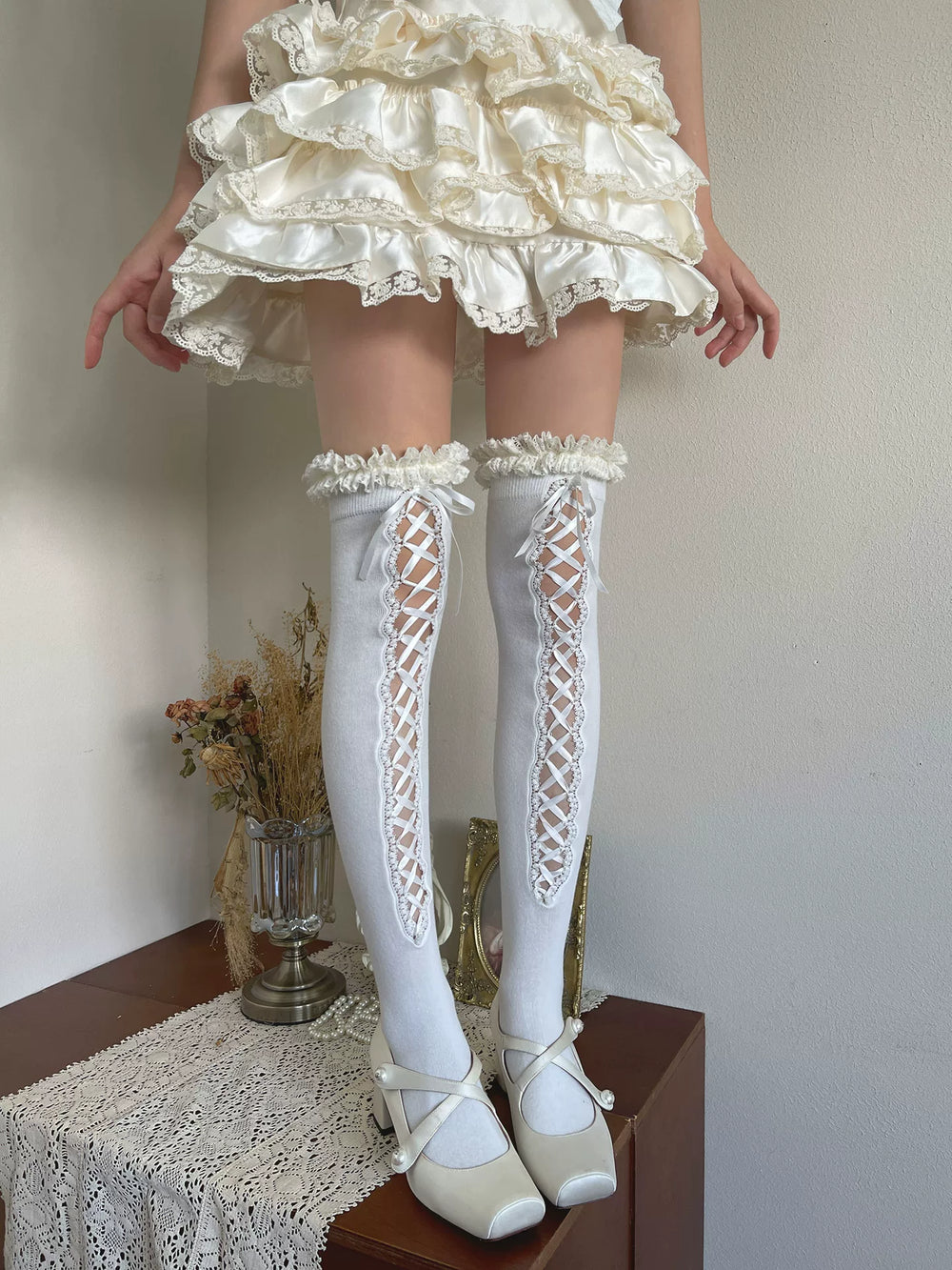 White lace-up thigh-high socks with ruffled tops styled with white shoes.