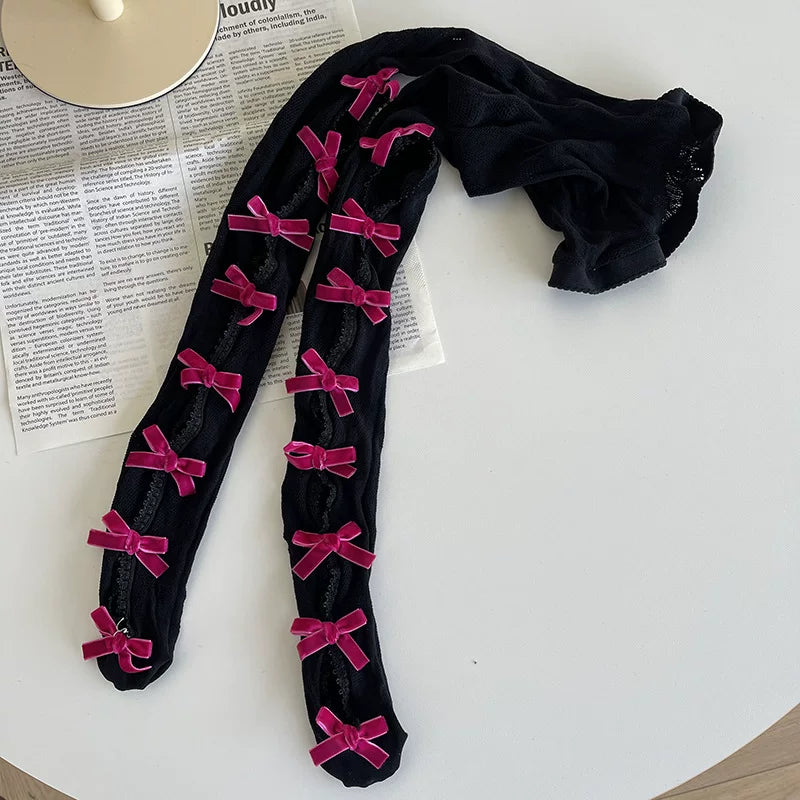 Black tights with repeated pink bows and openwork lace panels laid on a magazine.