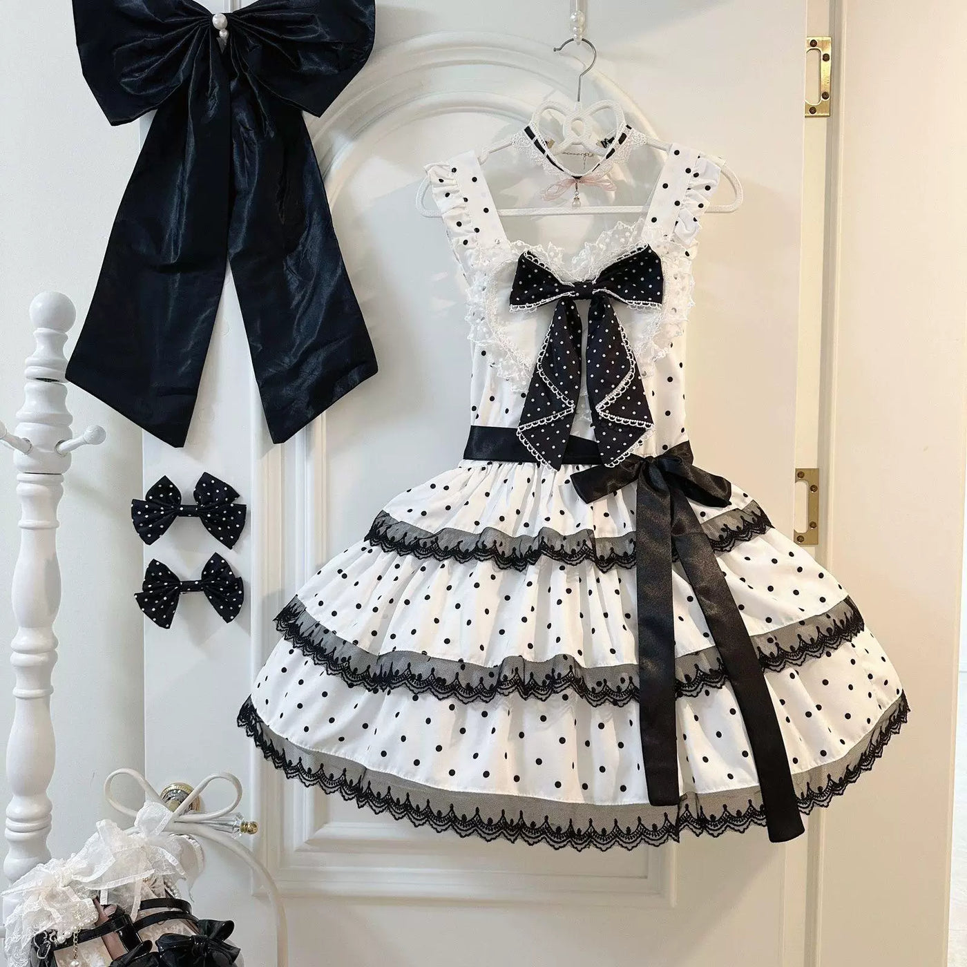 White polka-dot JSK dress with a large black bow and tiered lace trim displayed on a hanger.
