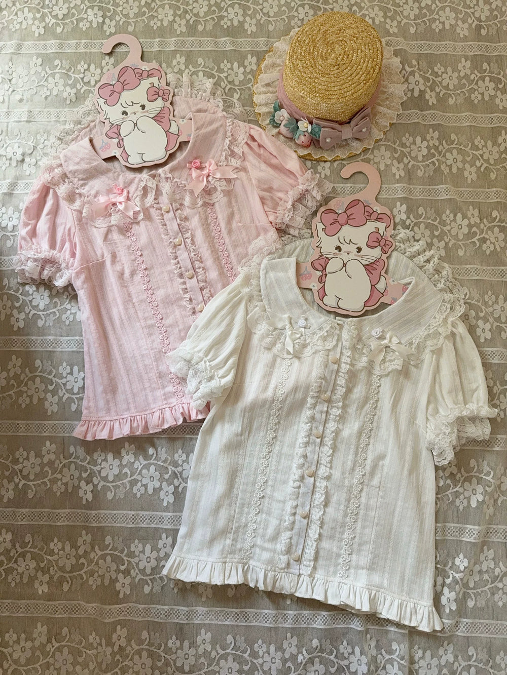 Pink and white blouses with lace trim, Peter Pan collars, and bow details laid on a floral textile.