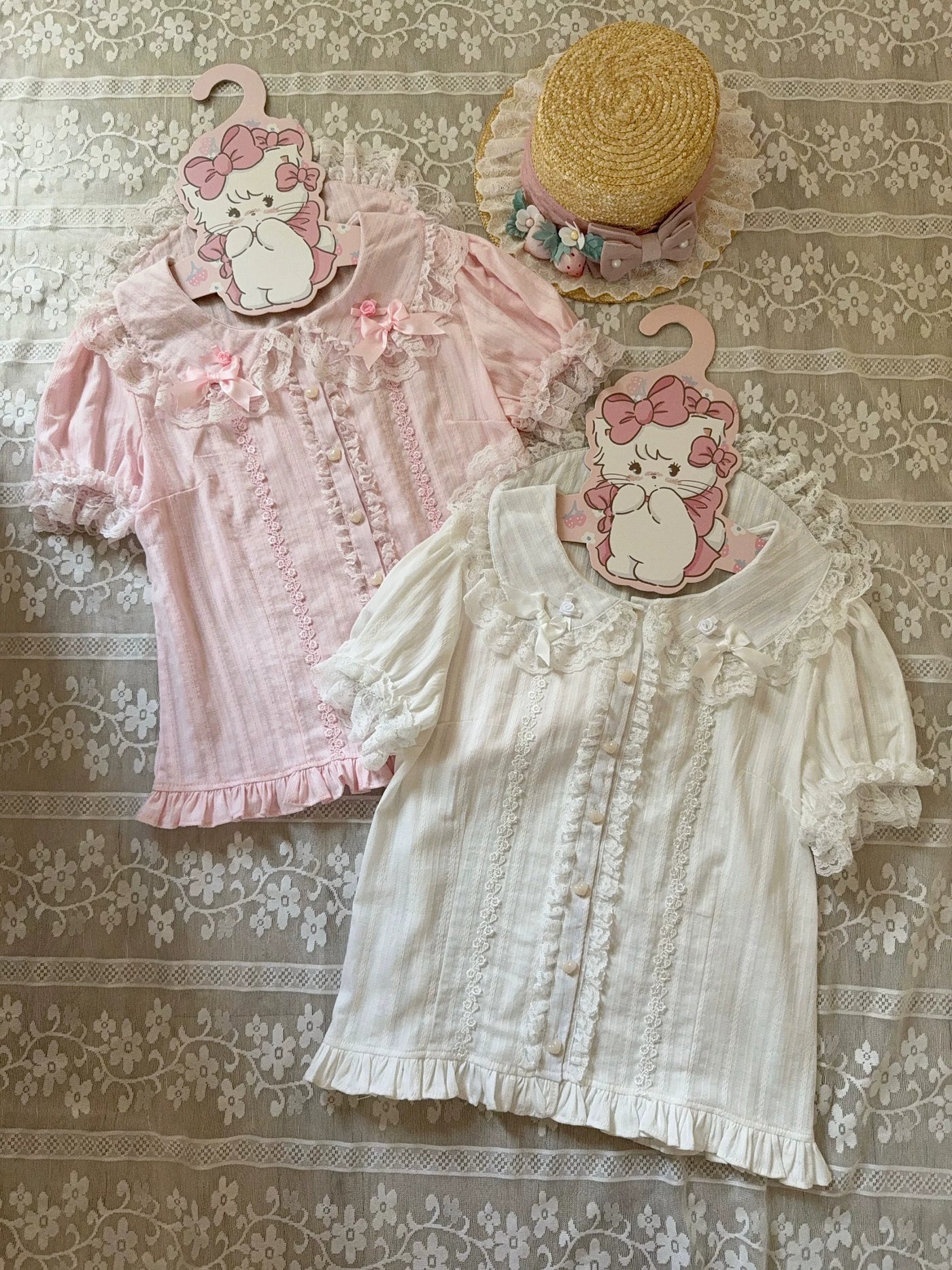 Pink and white blouses with lace trim, Peter Pan collars, and bow details laid on a floral textile.