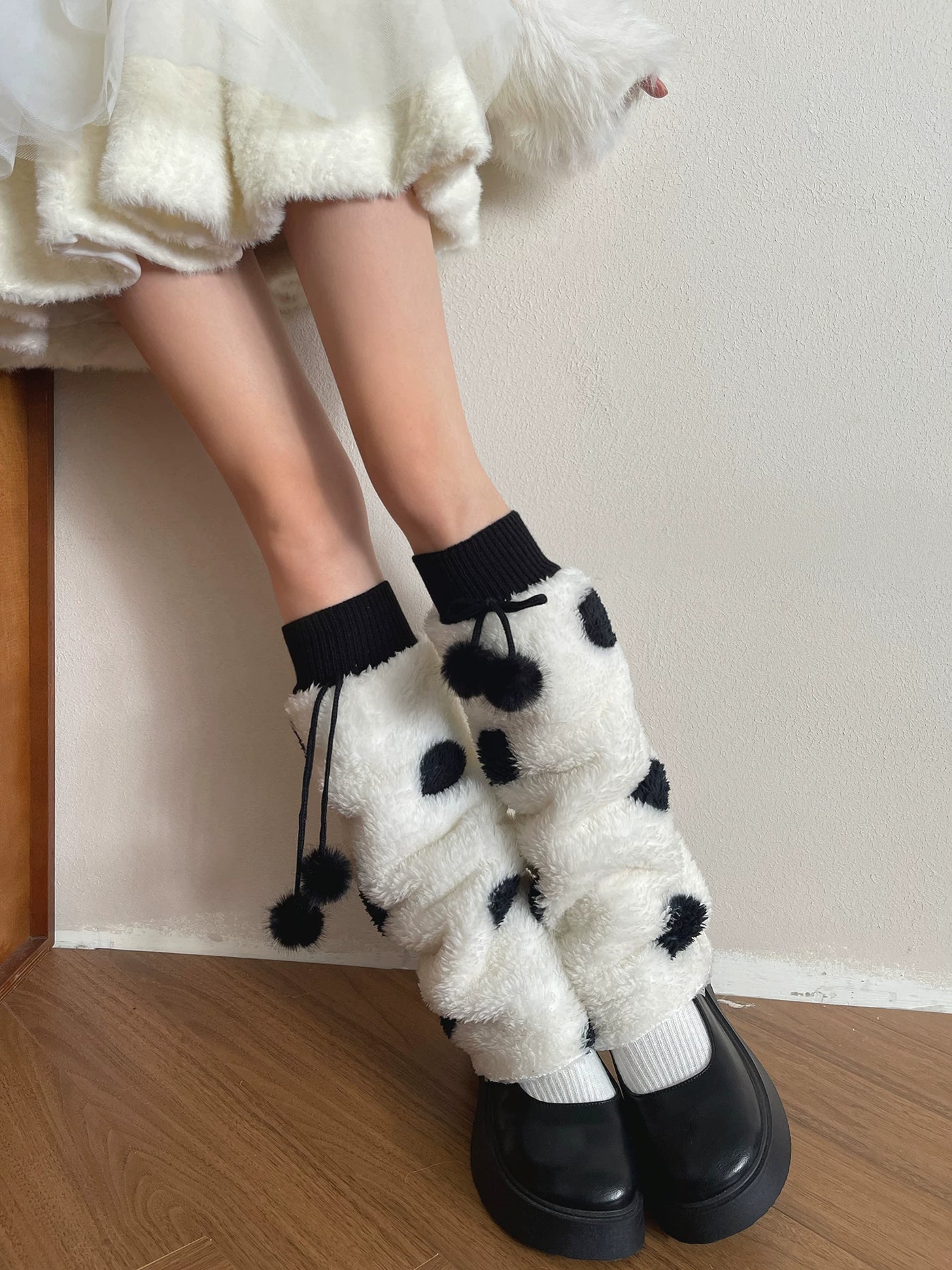 Model wearing fluffy cream sock covers with black polka dots and dangling pom-pom ties.