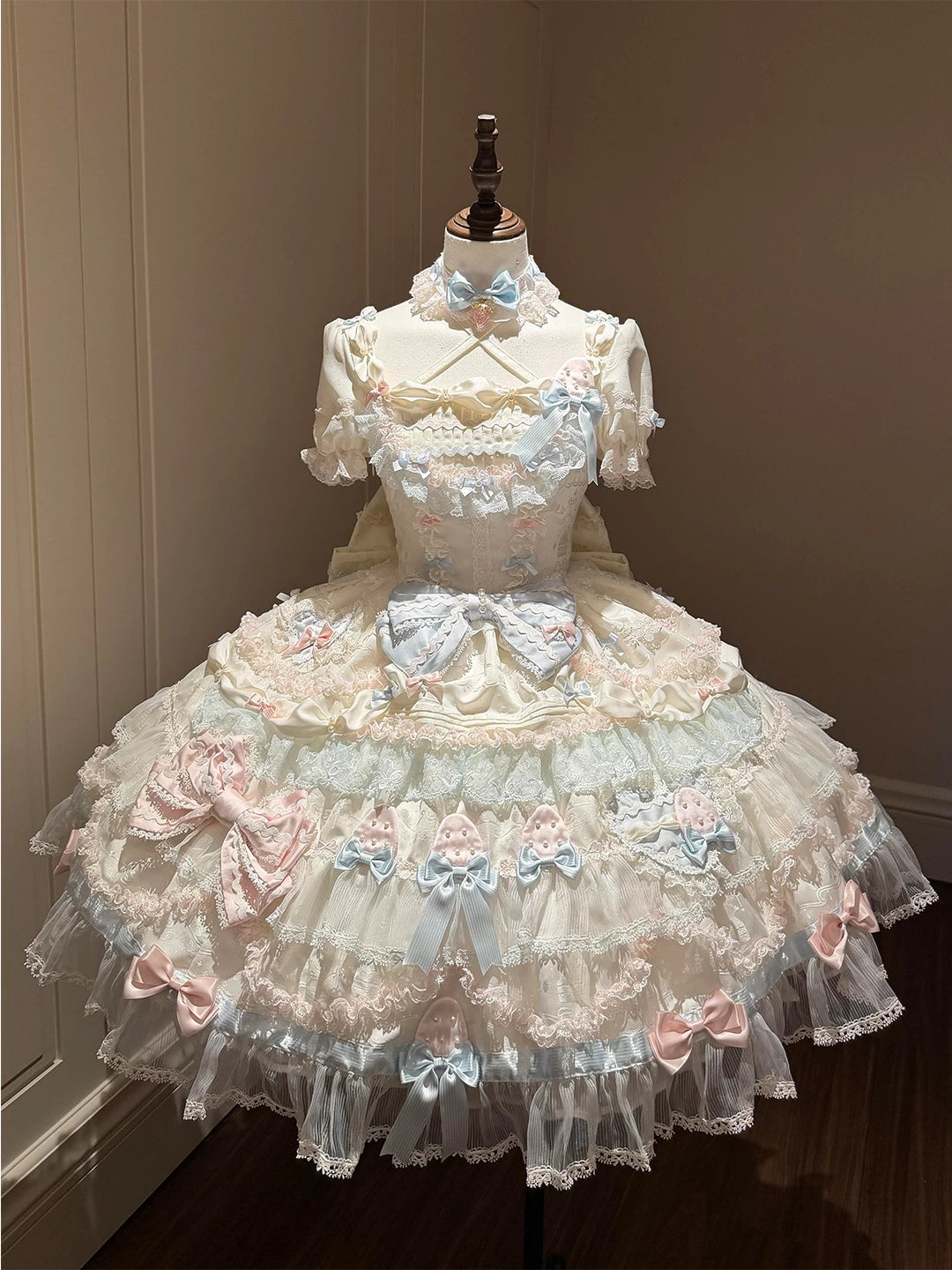 Pastel cream, blue and pink Lolita OP dress with layered lace tiers and a large train on a mannequin.