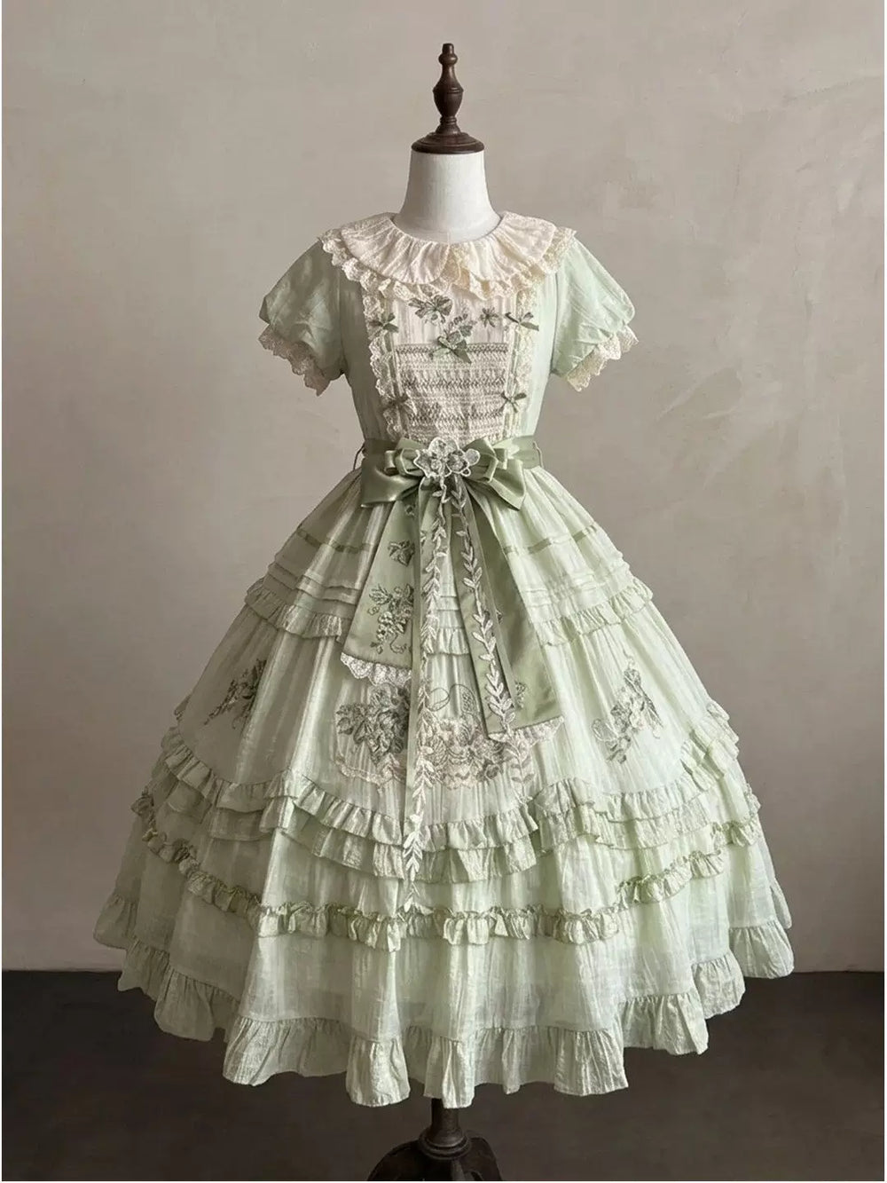 Pale sage green lolita OP dress with cream lace collar, puff sleeves, tiered mid-calf skirt, and sage green satin waist bow