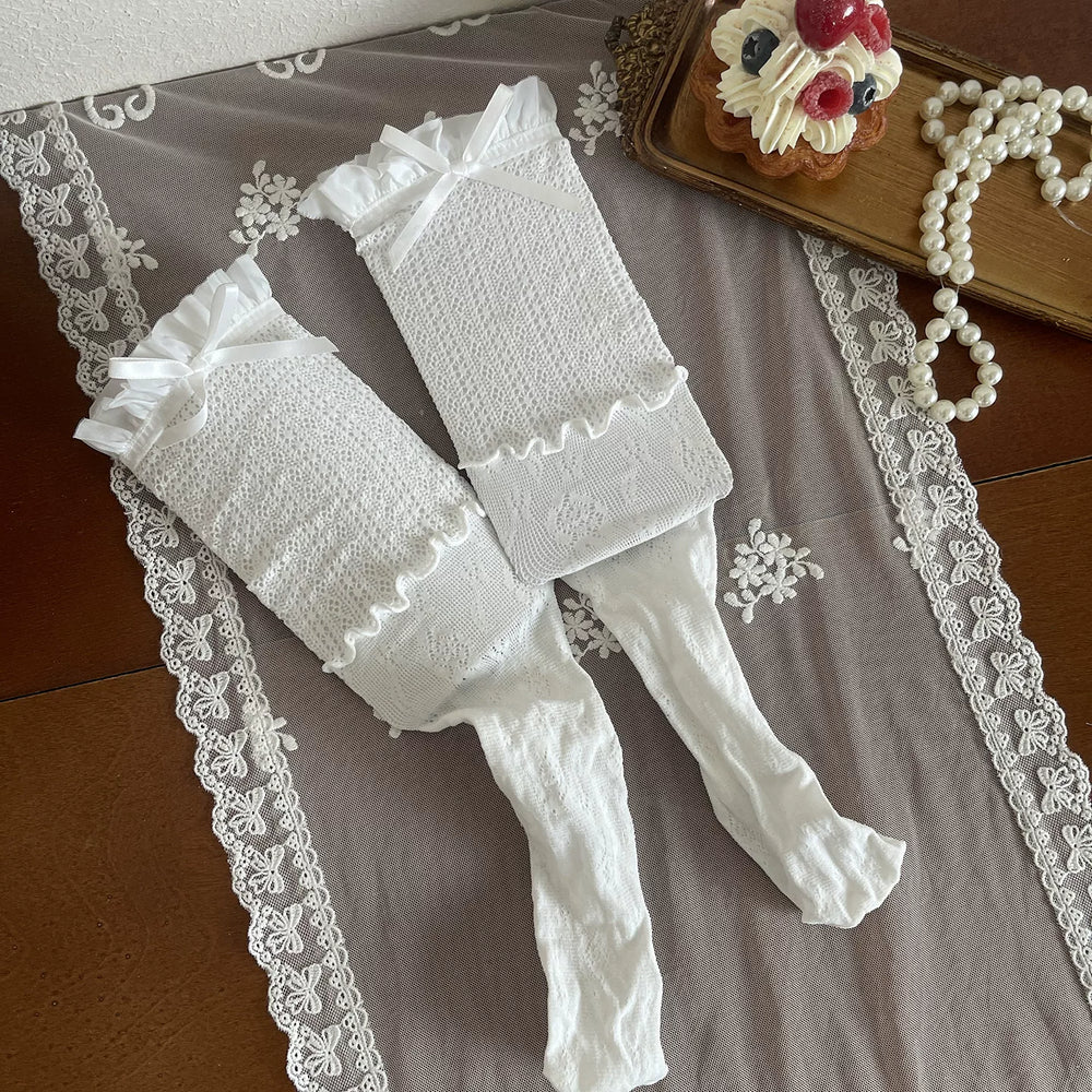 White lace stockings and legwear pieces with ribbon ties arranged flat on lace cloth.