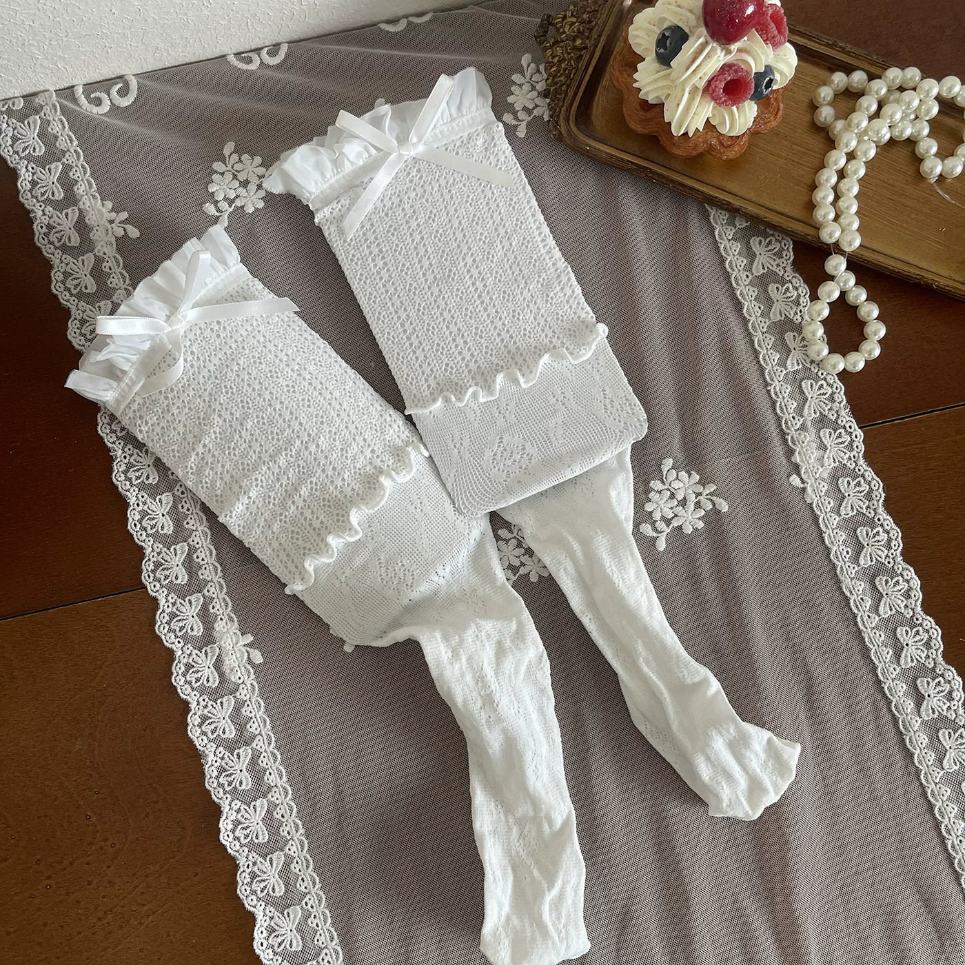 White lace stockings and legwear pieces with ribbon ties arranged flat on lace cloth.