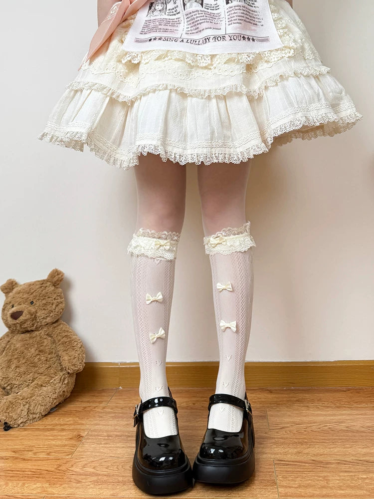White openwork slouch socks with lace trim and ribbon bows shown beneath a ruffled skirt.