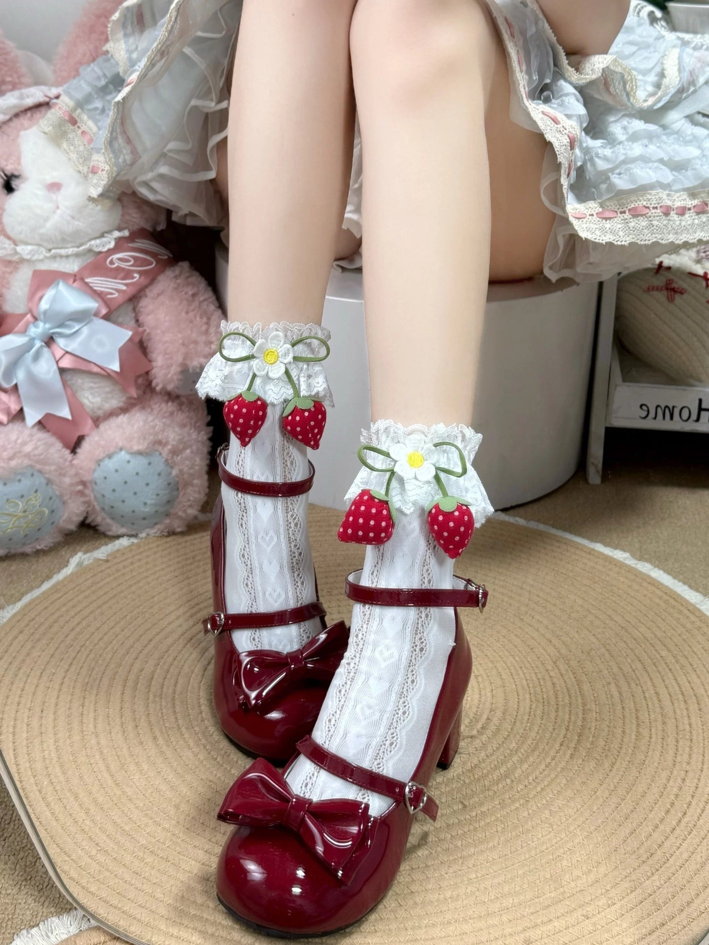 White lace mid-calf socks with strawberry accents and bows worn with burgundy Mary Jane shoes.