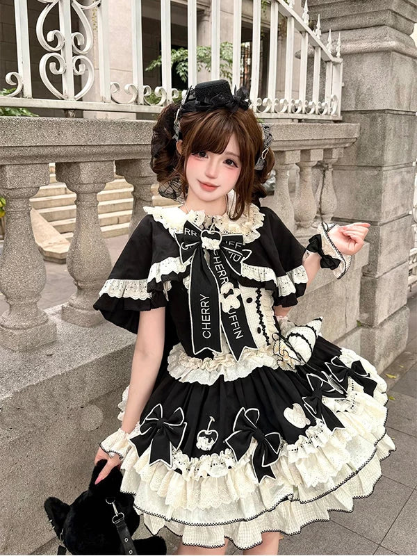 Model wearing a black JSK dress with cream frills, large bows and a cape.