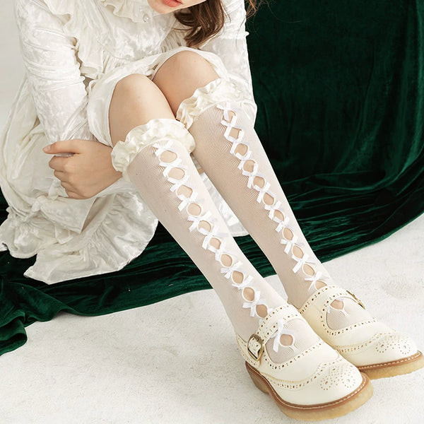 White mid-calf slouch socks with openwork lace panels and ribbon bows styled with white shoes.