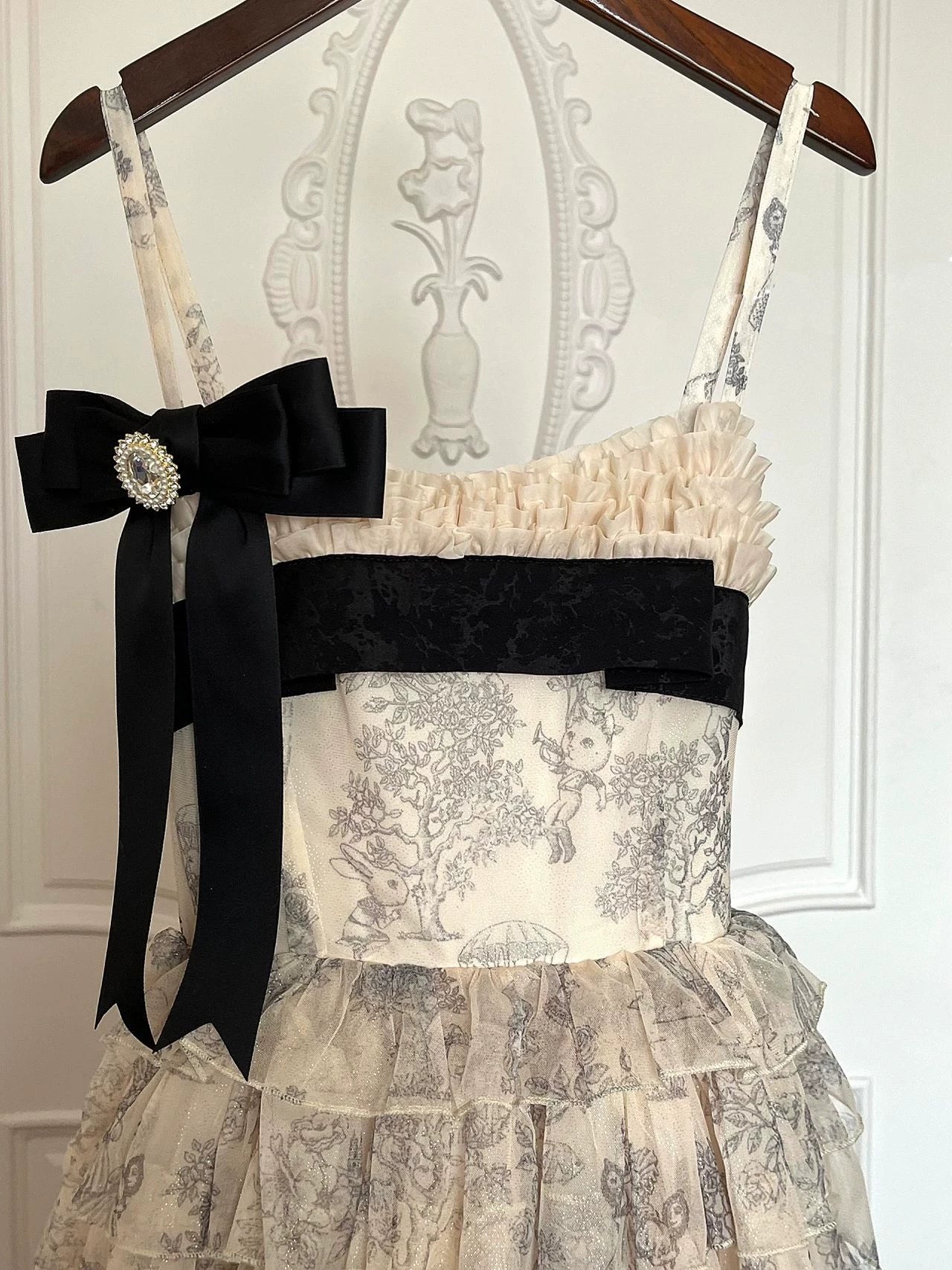 Cream-and-grey illustrated JSK dress with tiered ruffles and a large black bow on a hanger.