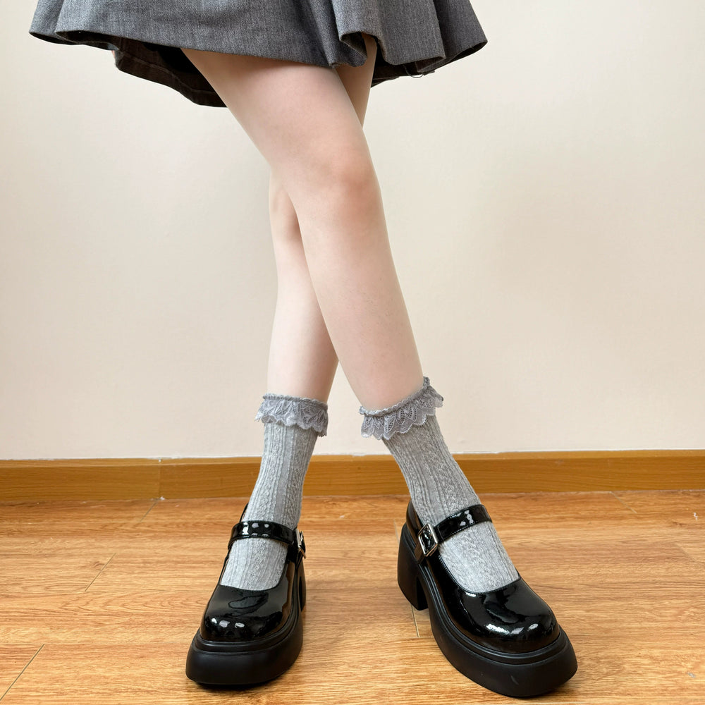 White and grey cable-knit mid-calf socks with lace trim styled with black Mary Jane shoes.