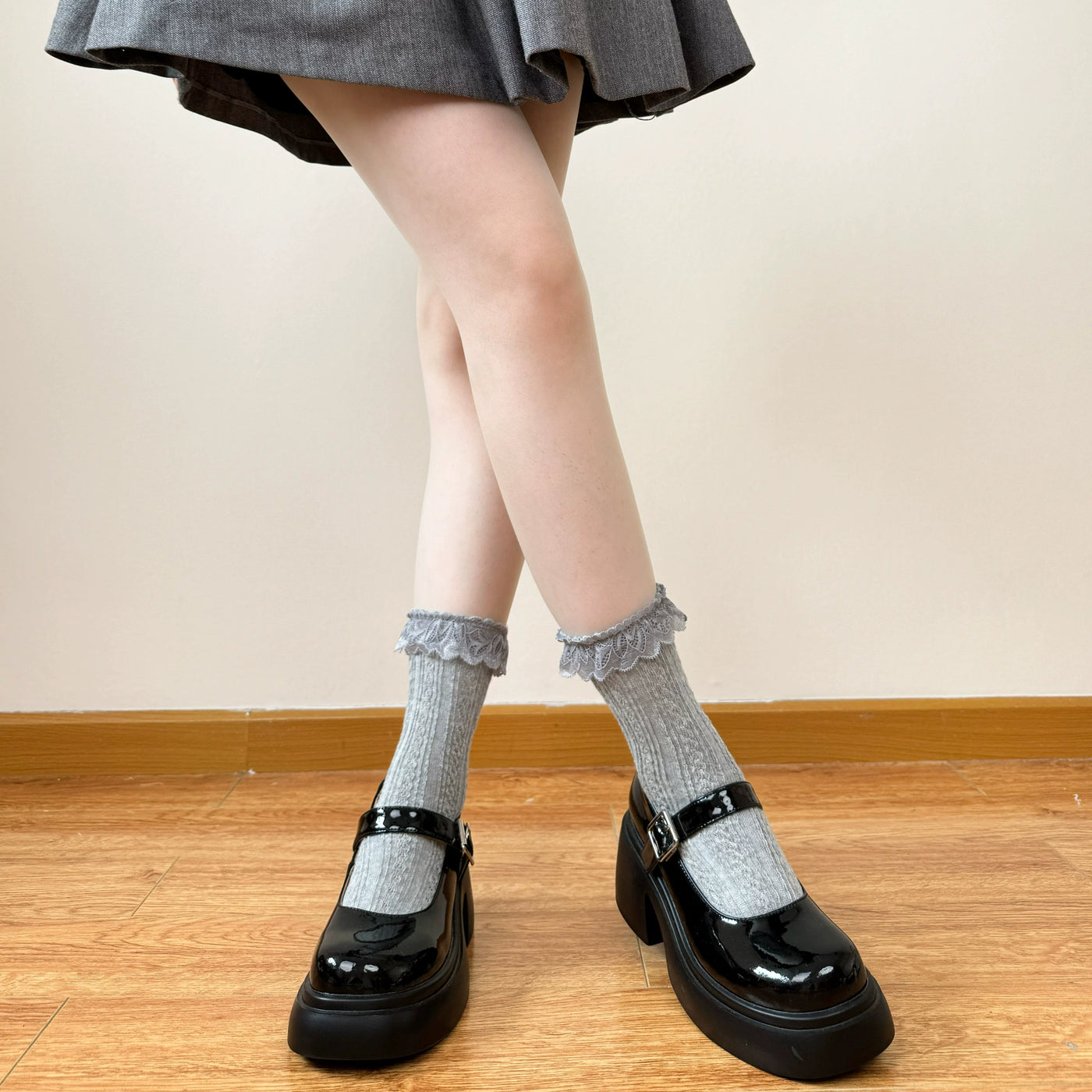 White and grey cable-knit mid-calf socks with lace trim styled with black Mary Jane shoes.