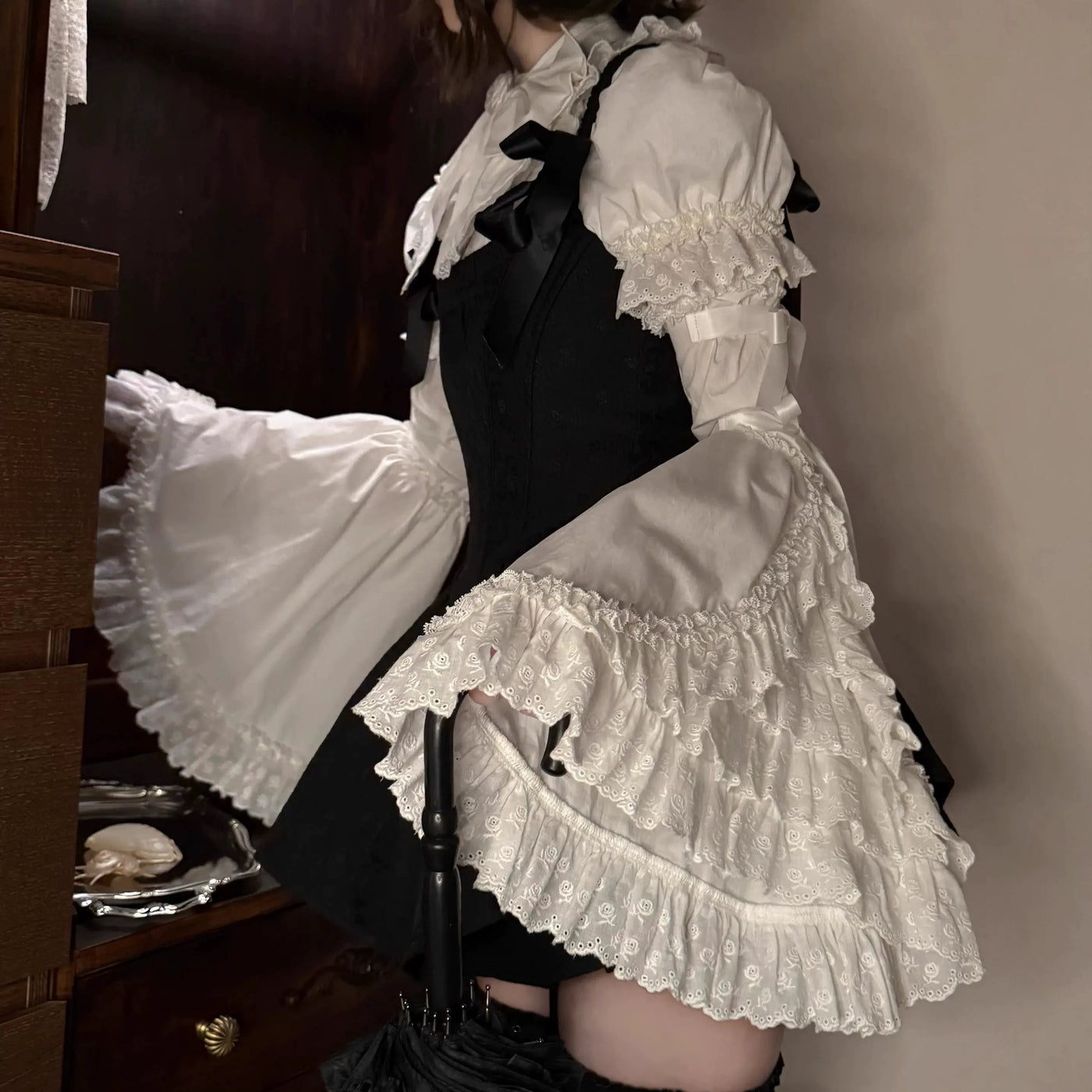 Black-and-white two-piece OP dress set with a fishbone-style bodice, white ruffled blouse and lace trim, shown on a model.