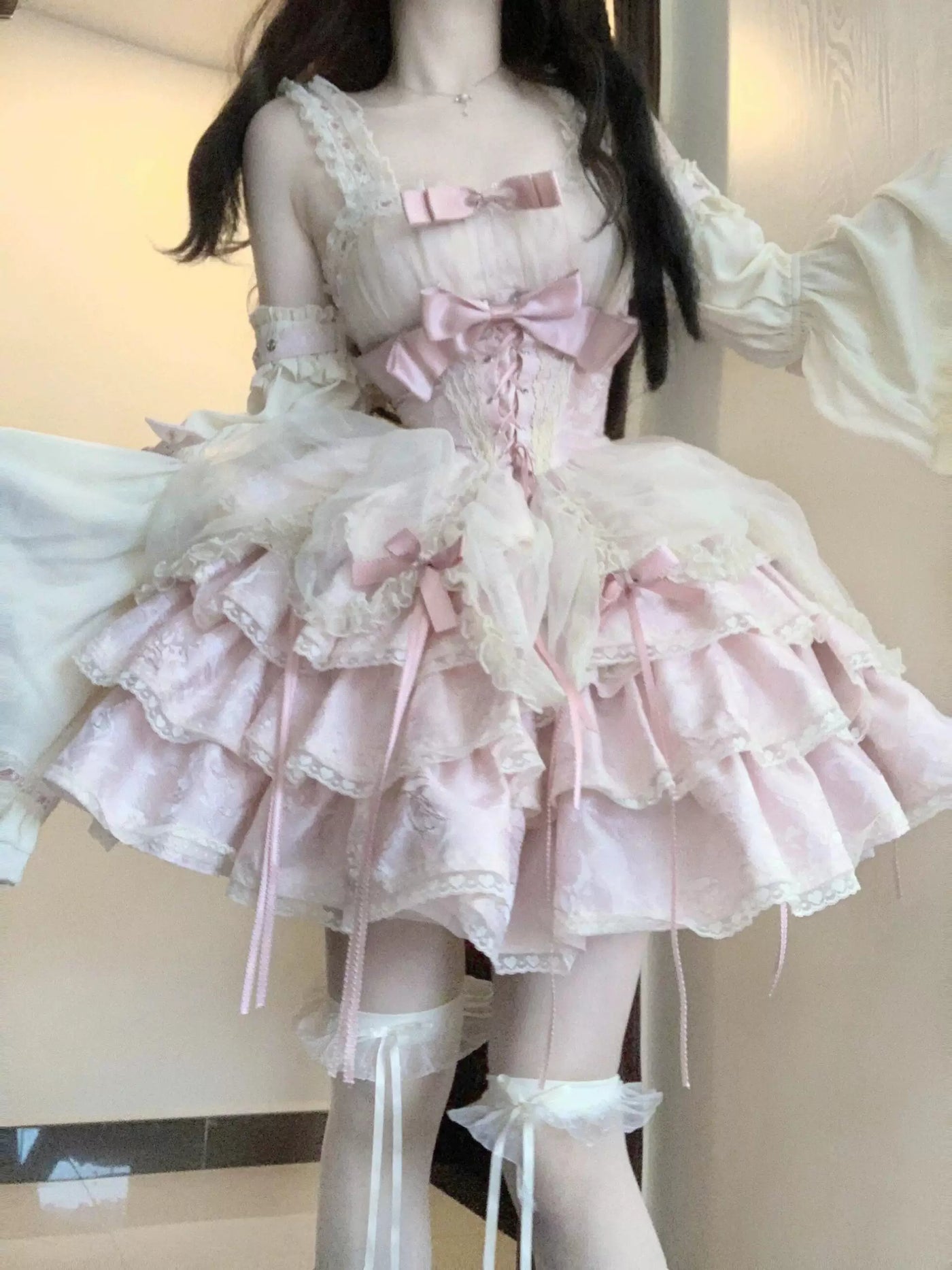 Pink ruffled JSK with lace straps, bow accents, corset-style lacing and matching hand sleeves worn by a model.