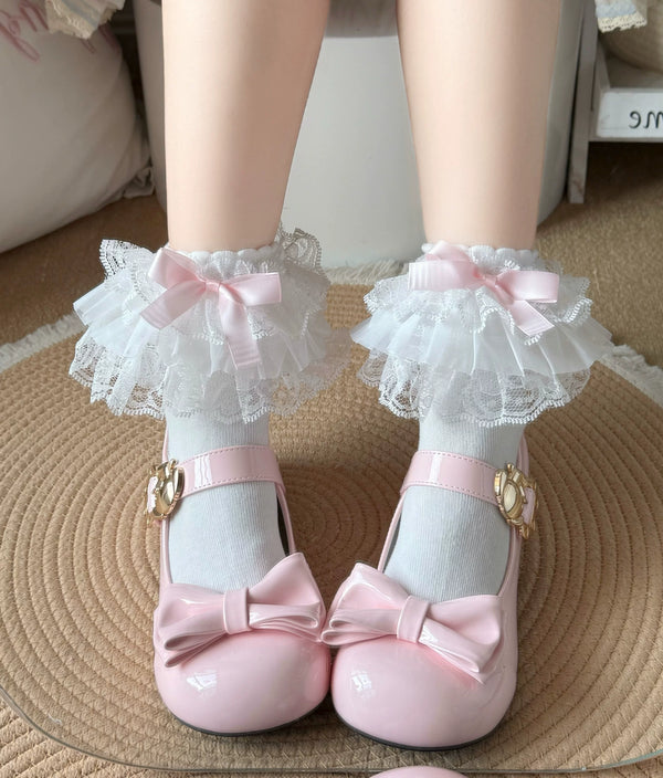 White lace-trimmed mid-calf socks with pink bows worn above glossy pink Mary Jane shoes.