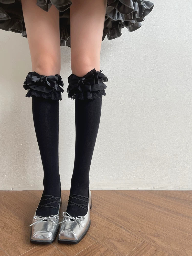 Black long socks with layered lace and bow trim paired with silver shoes.