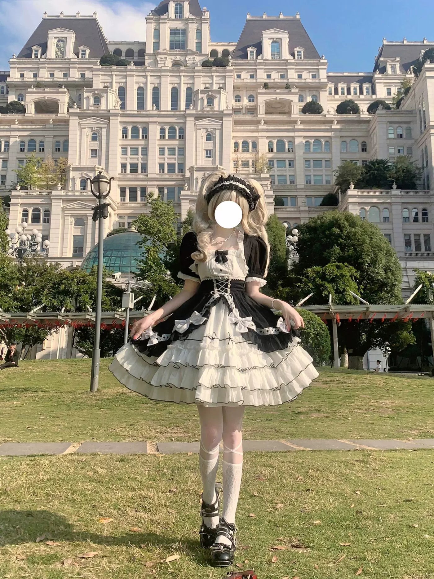 Black-and-white Lolita OP dress with white ruffles and bow accents styled outdoors.