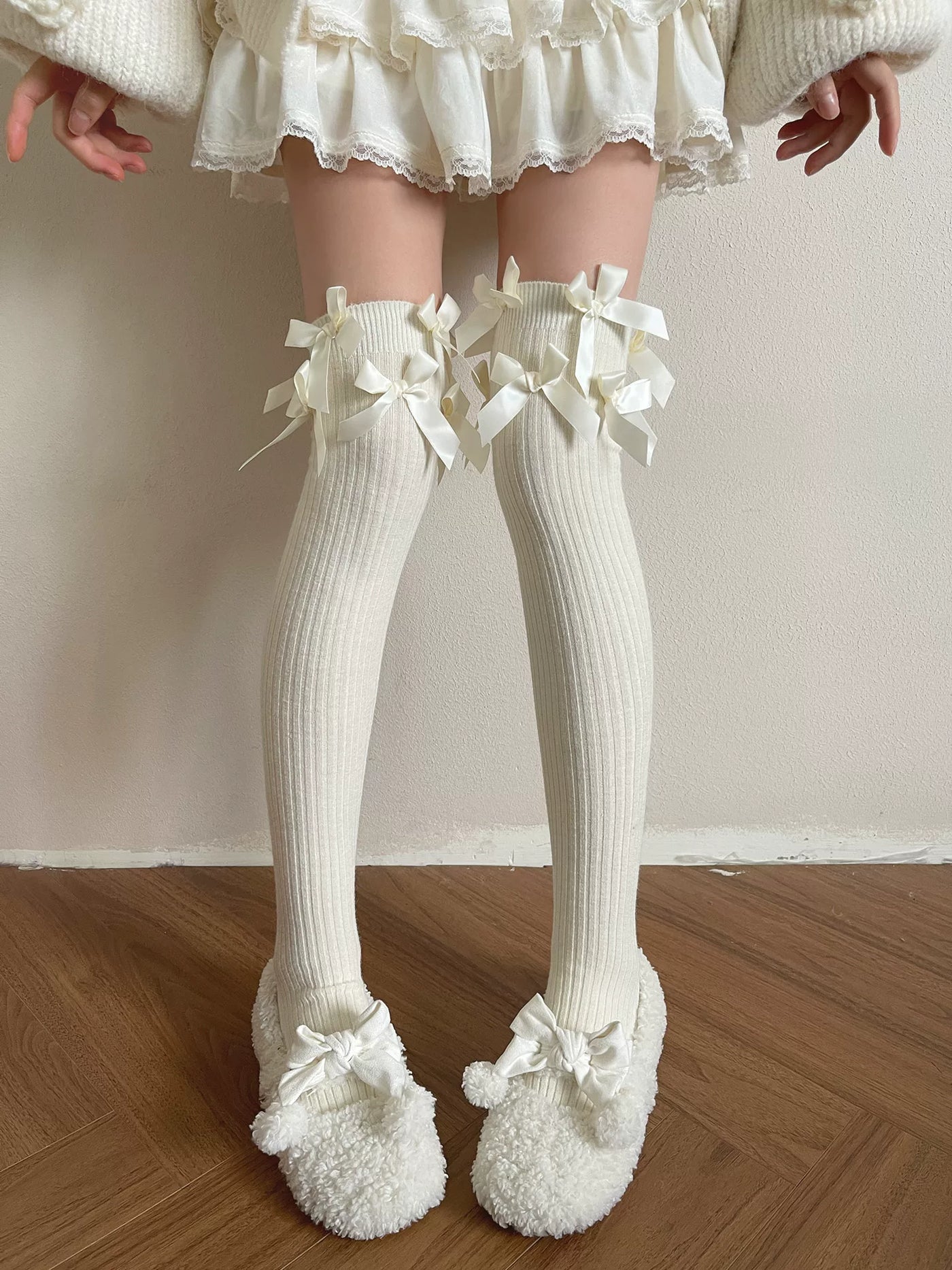 Model wearing milky white ribbed over-the-knee socks with satin bows beneath a lace-trimmed skirt.